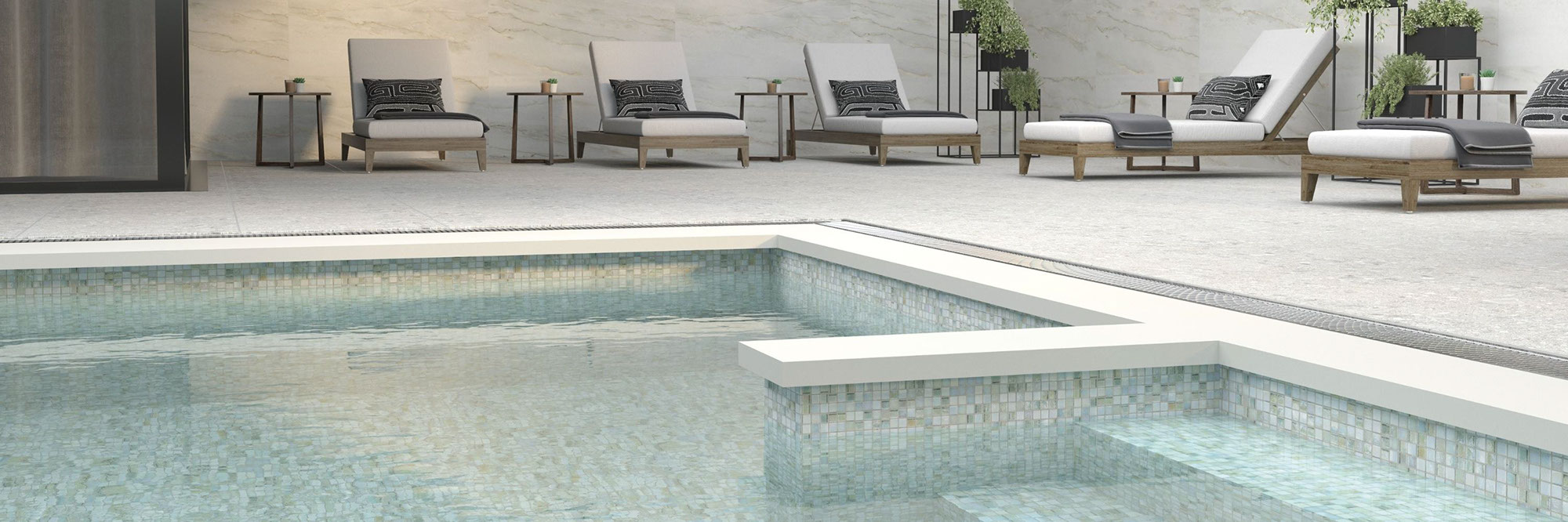 Outdoor pool with silver & gray mosaic pool tile, deck with white 2CM pavers, natural quartzite slab walls, and wooden lounge chairs with white cushions.