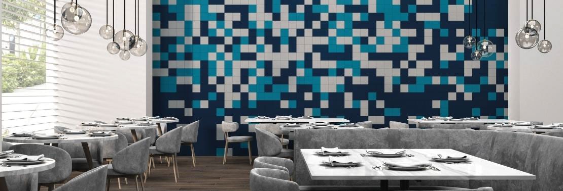 Restaurant dining room with 20-foot feature wall of navy, white, and teal tile in a random pattern, globe pendant lighting, wood look tile flooring, and tables with gray suede chairs & booths.