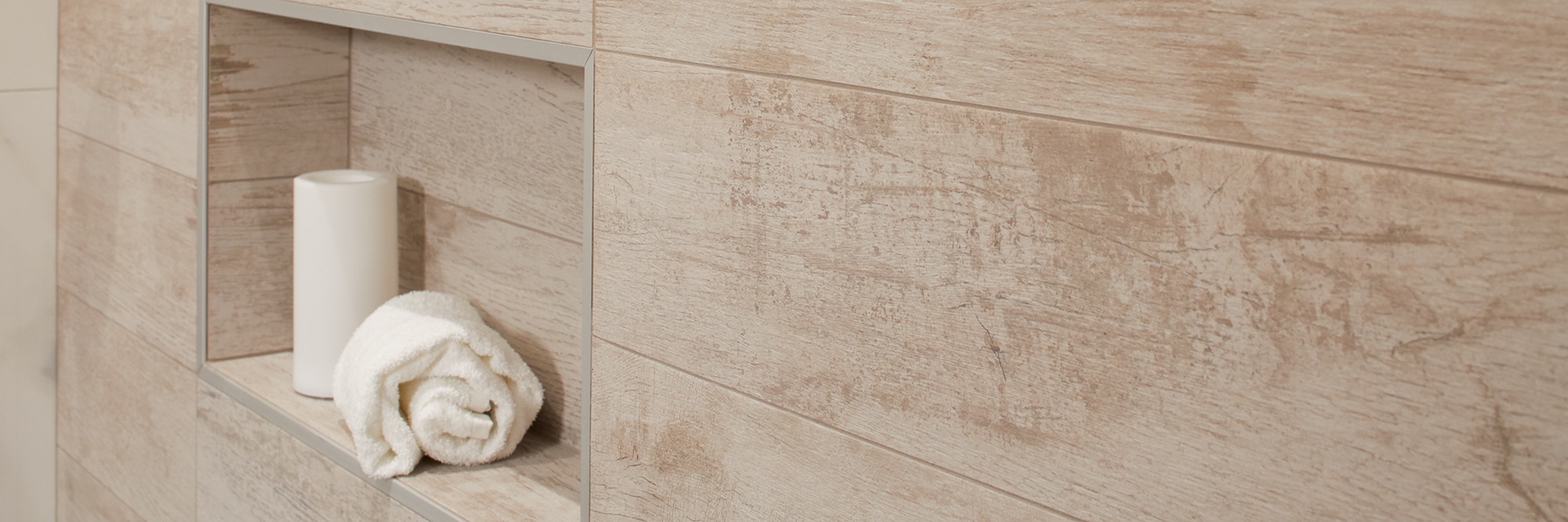 Closeup of shower wall tile that looks like white-washed wood with shower niche holding a rolled up towel.