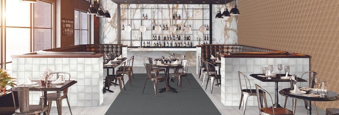 Restaurant/bar with white & beige marble backsplash, ceiling with exposed pipes & airducts, brass textured wall tile, white stone look & dark gray floor tile.