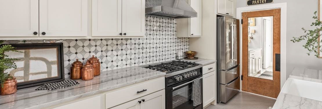 Renovated kitchen with gray natural quartzite countertops, black mirror and white & gray marble petal mosaic backsplash, white cabinets, and stainless steel appliances.