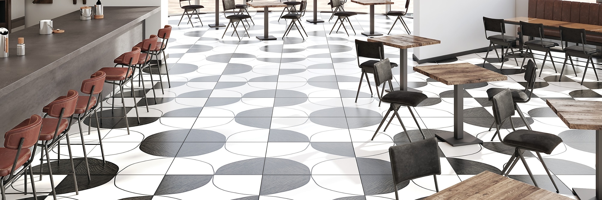 Restaurant with white floor tile with black circles & designs, wood tables with black chairs, gray porcelain slab countertop with maroon chairs.