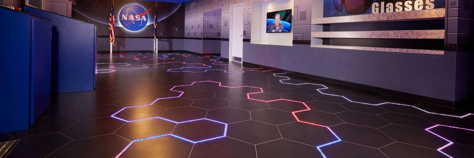 Kennedy Space Center Visitor Complex’s Astronaut Encounter Theater lobby with multi-colored neon string light intertwined throughout black hexagon floor tile.