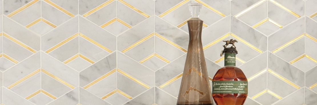 Closeup of gray marble and antique brass mosaic wall tile, brown decanter, and bottle of alcohol.