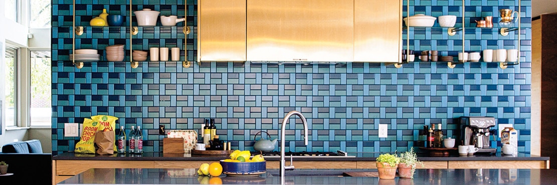 Kitchenette with light and dark blue mosaic backsplash, open shelving, copper vent hood over gas stove, black quartz countertops and island.