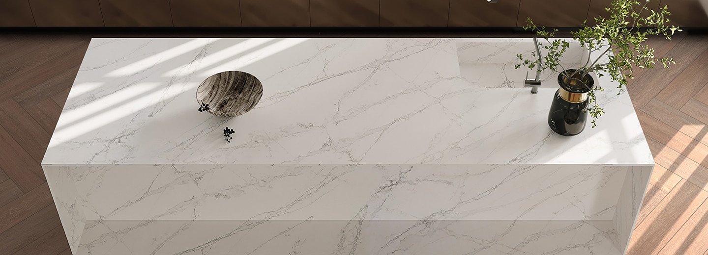Kitchen with center island with white marble countertop and light wood floor.