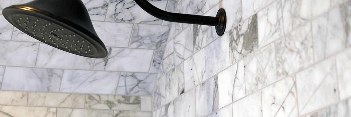 Closeup of white marble gray veining shower tile and matte black showerhead.