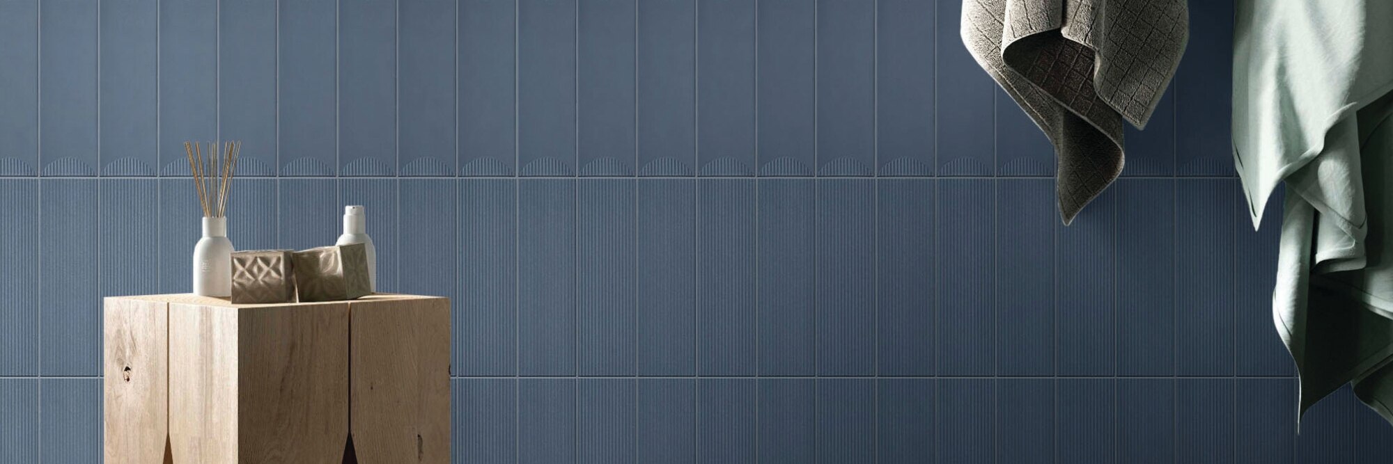 Blue textured wall tile, small wooden table, with gray and mint green towels hanging on hooks.