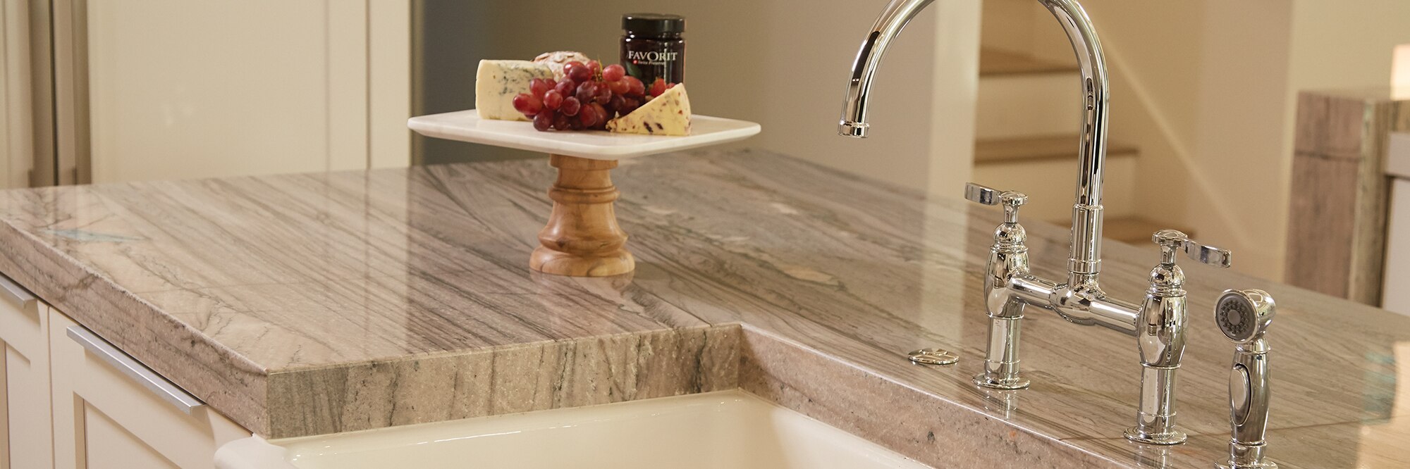 Closeup of kitchen island of tan quartzite countertop with black veining, built in sink, polished silver faucet, and tray of fruit and cheese.
