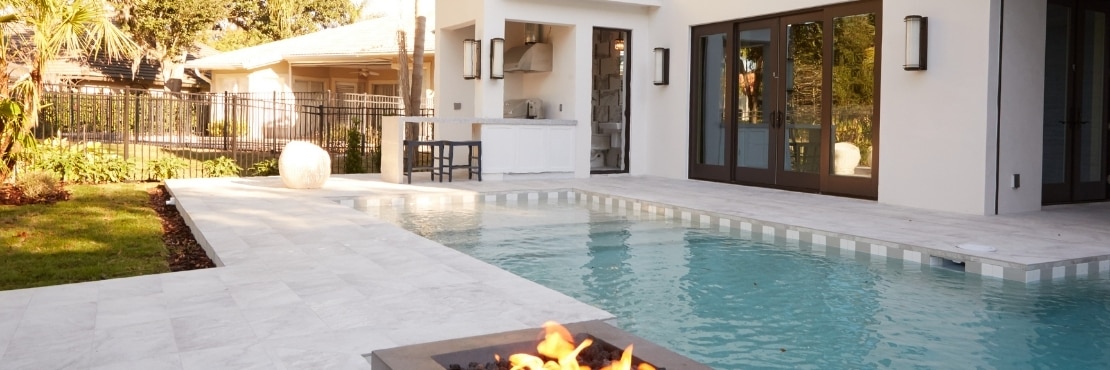 Backyard of white stucco house with outdoor kitchen, firepit, pool with white  & gray waterline tile and white stone look tile deck.