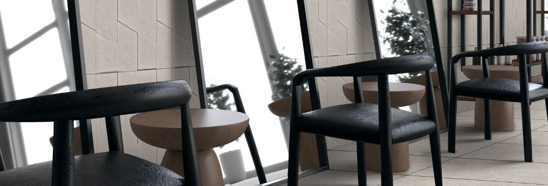 Hair salon with stone look beige textured wall tile and large format stone look beige floor tile, black chairs, and tall mirrors leaning against the wall.