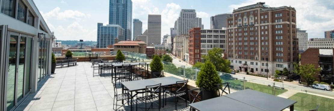 Rooftop restaurant with light beige limestone look 2CM porcelain pavers under black tables & chair with skyscrapers and blue skies in the background.