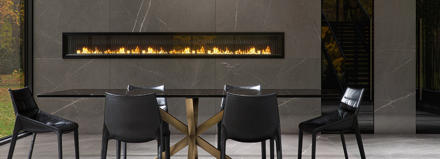 High end dining room with a black table and black chairs, fireplace in the back wall, and gray marble look slab on the back wall and floors.
