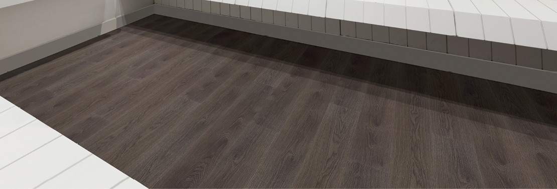 Closeup of locker room floor with luxury vinyl tile that looks like dark wood flooring and white wood benches.