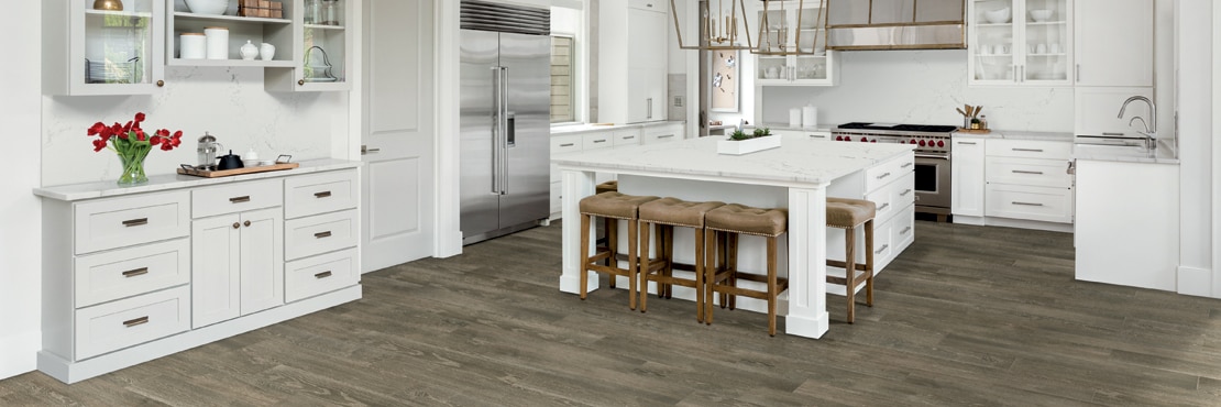 Transitional kitchen with floor tile that looks like wood, white cabinets, white quartz with gray veining countertops, island, and backsplash.