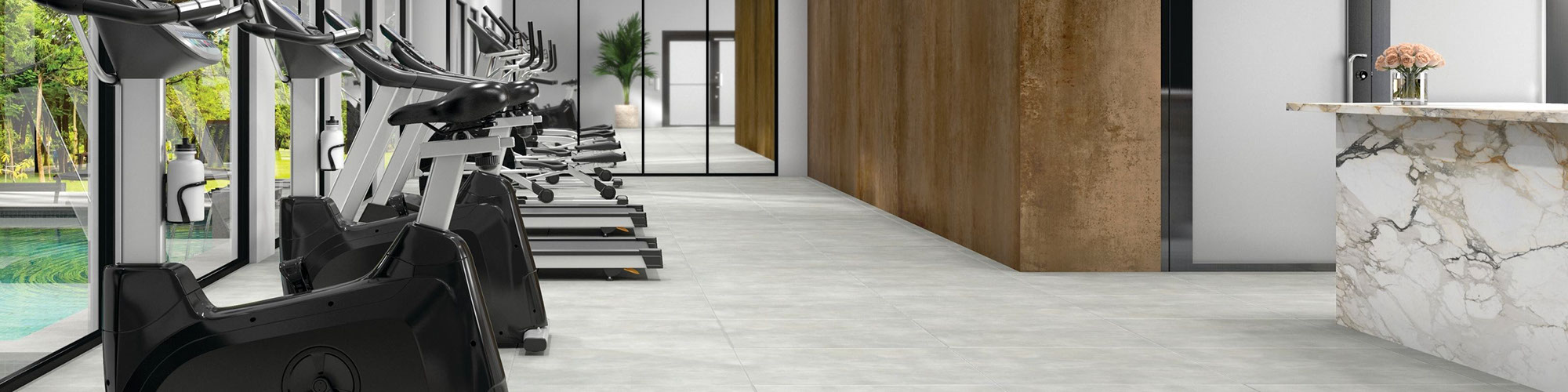 Hotel gym with a row of treadmills and stationary bicycles, stone look gray tile floor, metal look bronze wall tile, and white & gray marble look porcelain slab countertop.