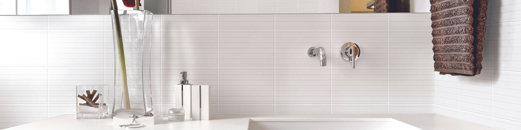 Clean-lined white bathroom with larger white subway tile in a grid pattern on the wall. Red orchid in pot on the white quartz vanity.