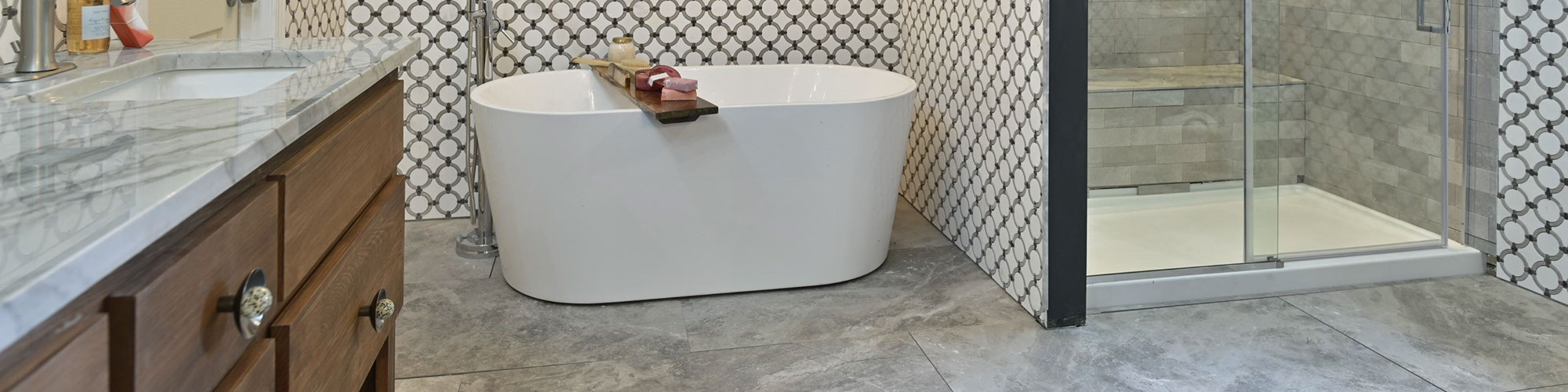 Bathroom with free standing bathtub in front of wainscoting of white marble tile with gray rings and shower with gray tile and niche with matching marble tile with rings.