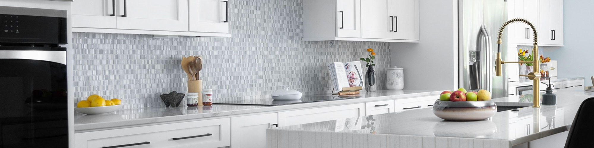 White kitchen design with tan & gray natural quartzite countertop, white cabinets with silver handles, beige & white glass mosaic backsplash.
