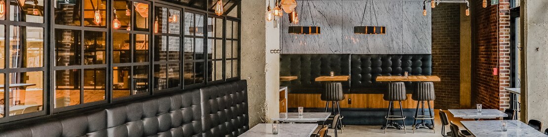 Restaurant dining room with heavy veining gray marble tabletops and wall tile, booths with tufted black leather back, and specialty pendant lighting.