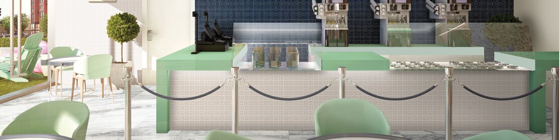 Ice cream parlor with marble look tile flooring, 3 ice cream dispensers, navy mosaic backsplash, beige & mint-colored counter, tables, and chairs.