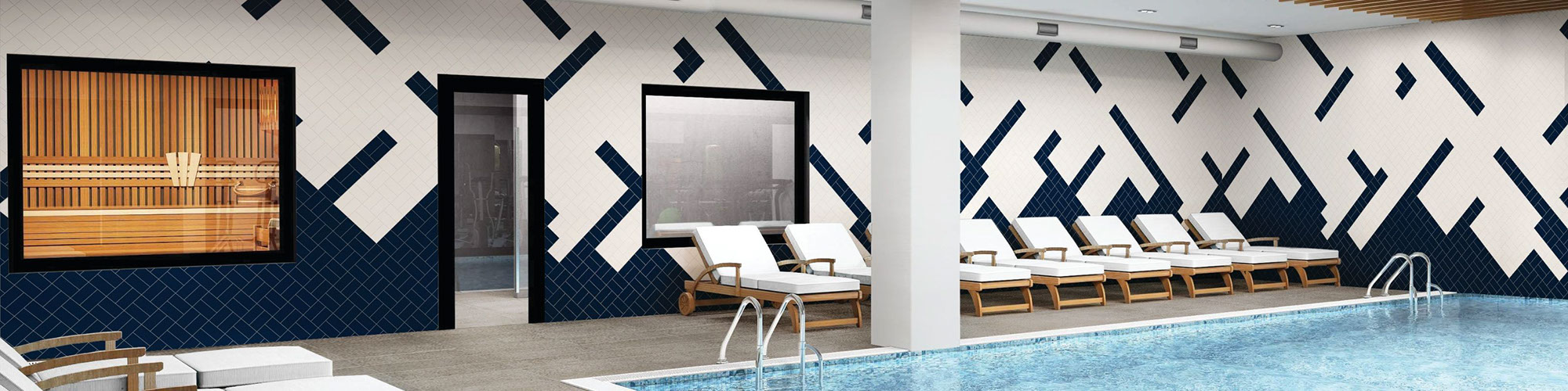 Indoor hotel pool with gray concrete look tile deck, wood lounge chairs with white cushions, and white & navy wall tile in random pattern.