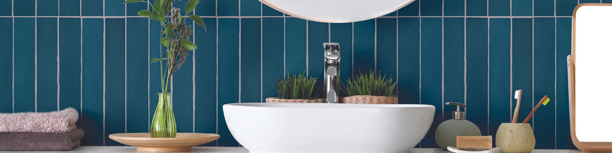 Bathroom vanity with vessel sink, blue tile backsplash laid in a vertical pattern, silver polished faucet, succulents in wicker baskets, soap dispenser and soap dish.
