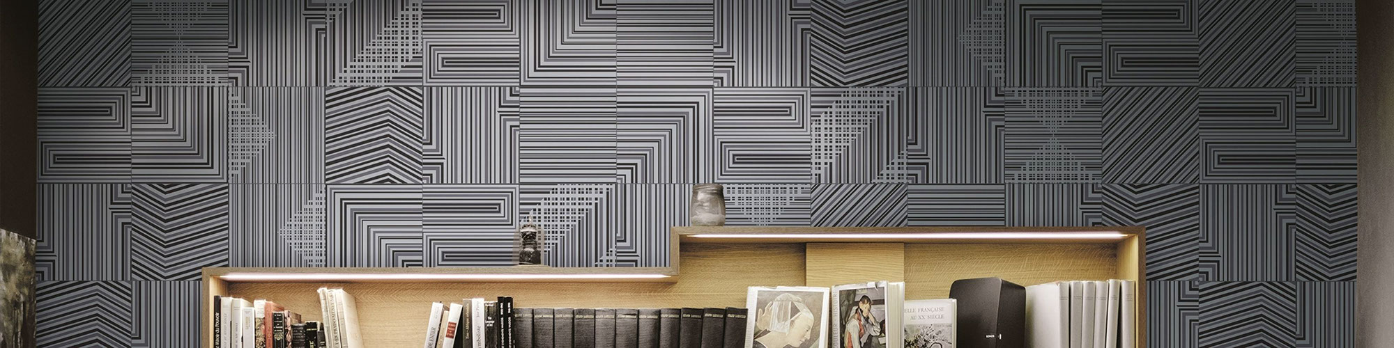 Metallic-look, geometric pattern tile on a library wall and light wood bookshelves with books.