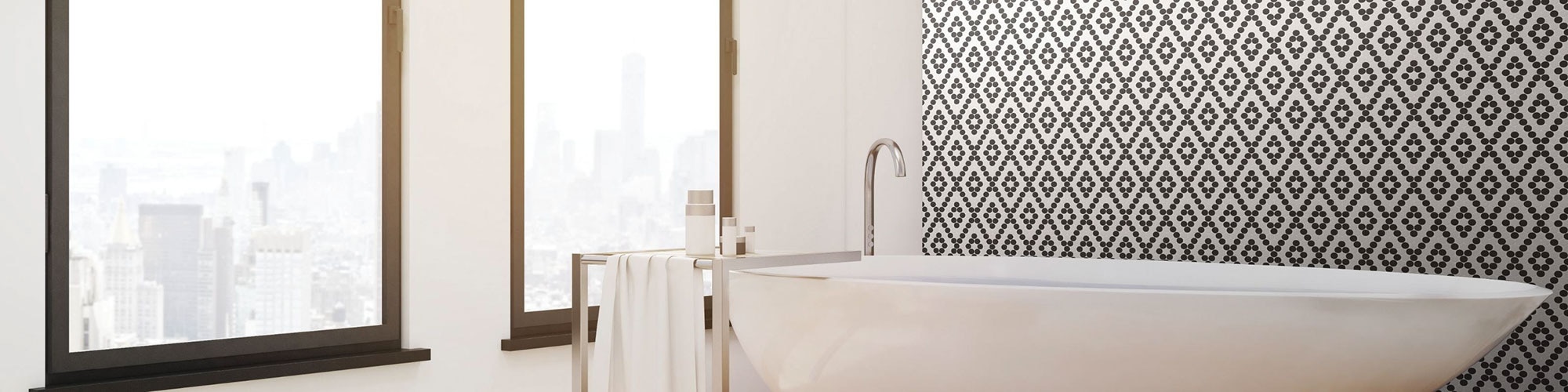 White, long soaker bathtub in front of a large picture window and black & white mosaic feature wall.
