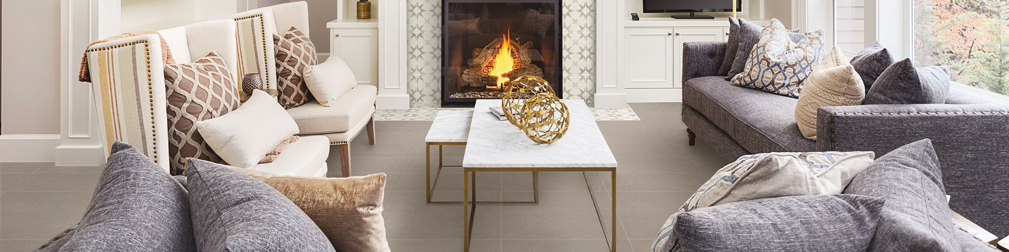 Living room with white built-ins, fireplace with off-white & gray encaustic tile, gray stone look flooring tiles, gray couch, and marble coffee table.