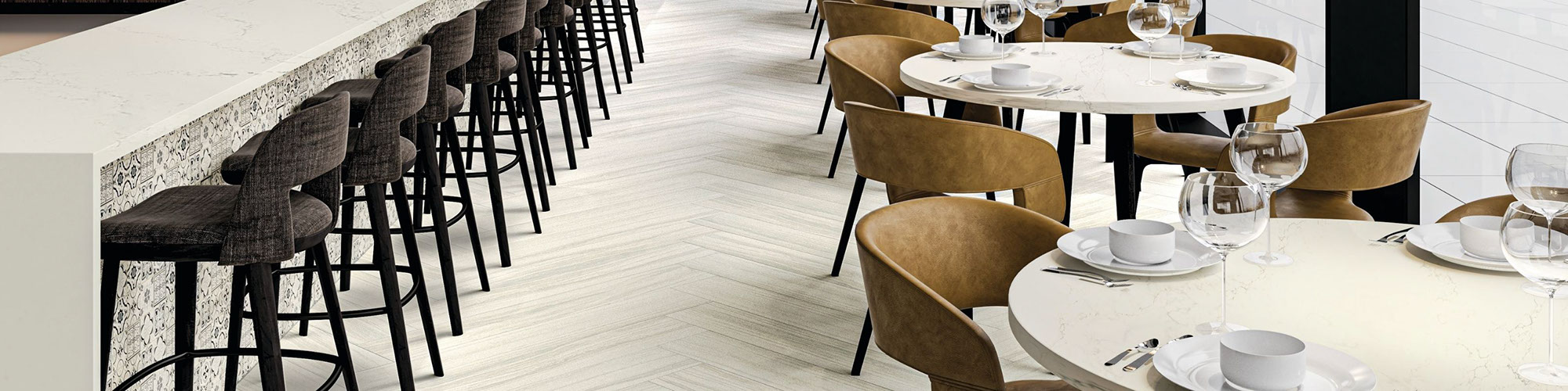 Restaurant with off-white stone look floor tile in a herringbone pattern, white quartz countertop and white & black encaustic, tables & chairs.