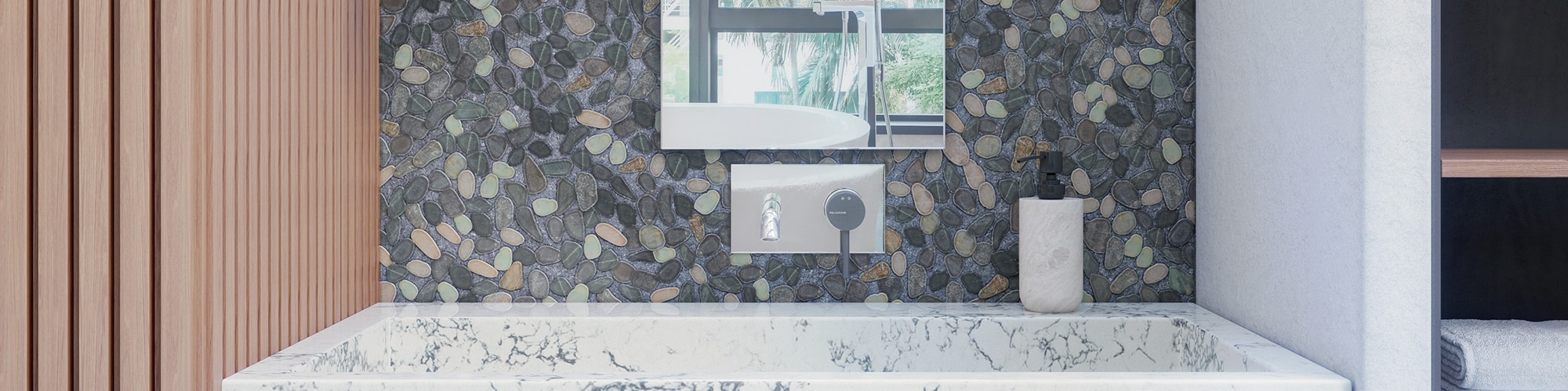 Bathroom vanity with gray pebble mosaic backsplash, mirror, polished silver wall-mounted faucet, white & gray quartz sink, and stone soap dispenser. 