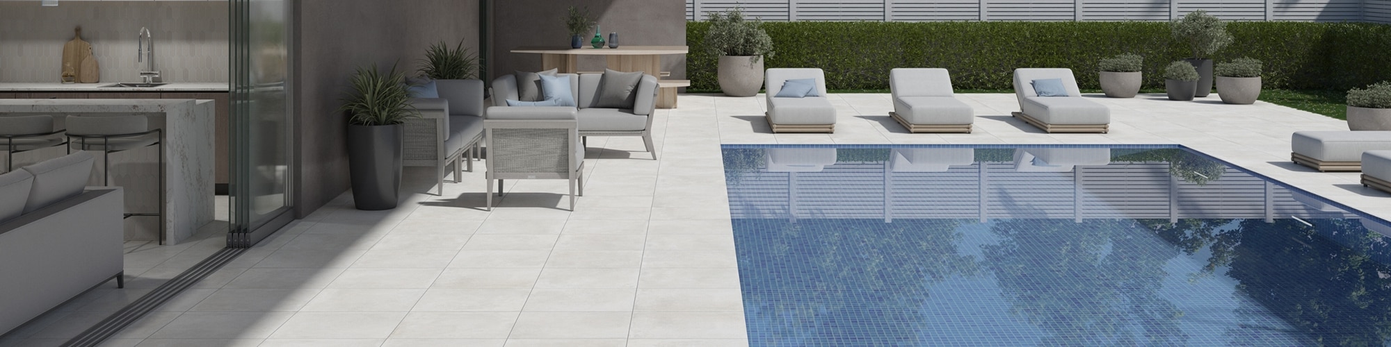 Modern home backyard with white marble look paver pool deck, pool with blue mosaic tile, gray seating area under patio cover, and cushioned lounge chairs.