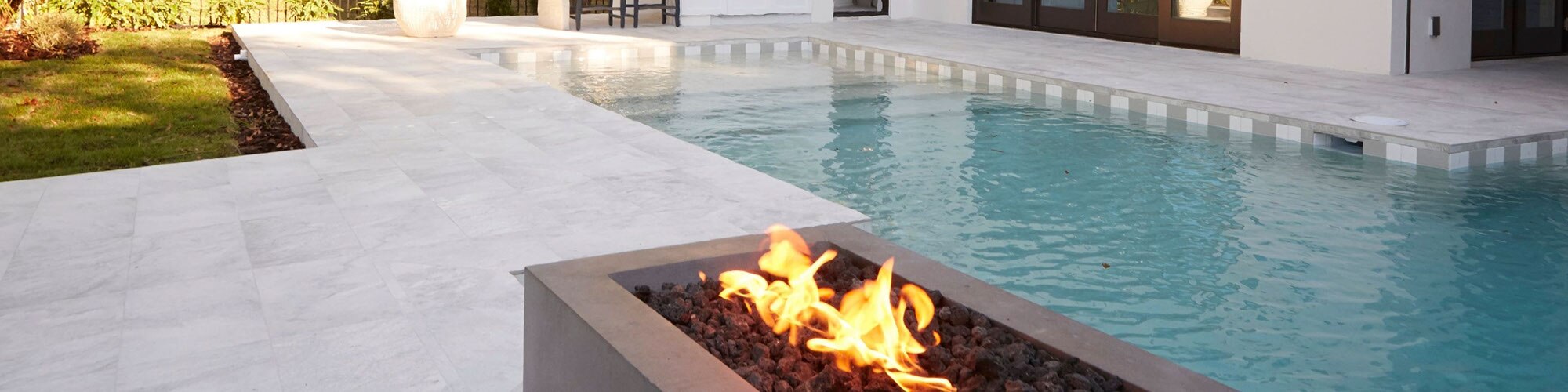 Backyard of house with firepit, pool with white & gray waterline tile and white stone look tile deck.
