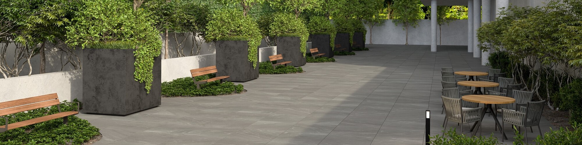 Office building courtyard with gray porcelain pavers that look like stone, dining table & chairs, wooden benches and large planters along white retaining wall. 