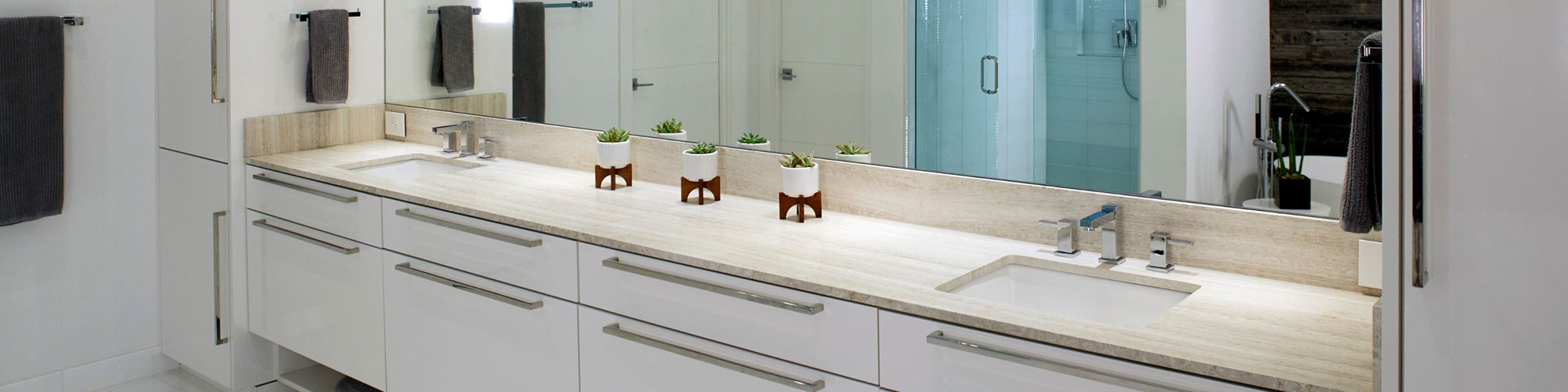Modern bathroom design with limestone countertop vanity, white cabinets, silver drawer pulls, and 3 small succulents in planters.