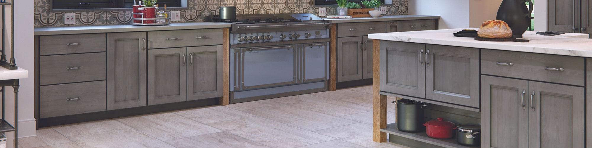 Country style kitchen with gray & beige encaustic wall tile, floor tile that looks like wood, and gray porcelain slab countertops.