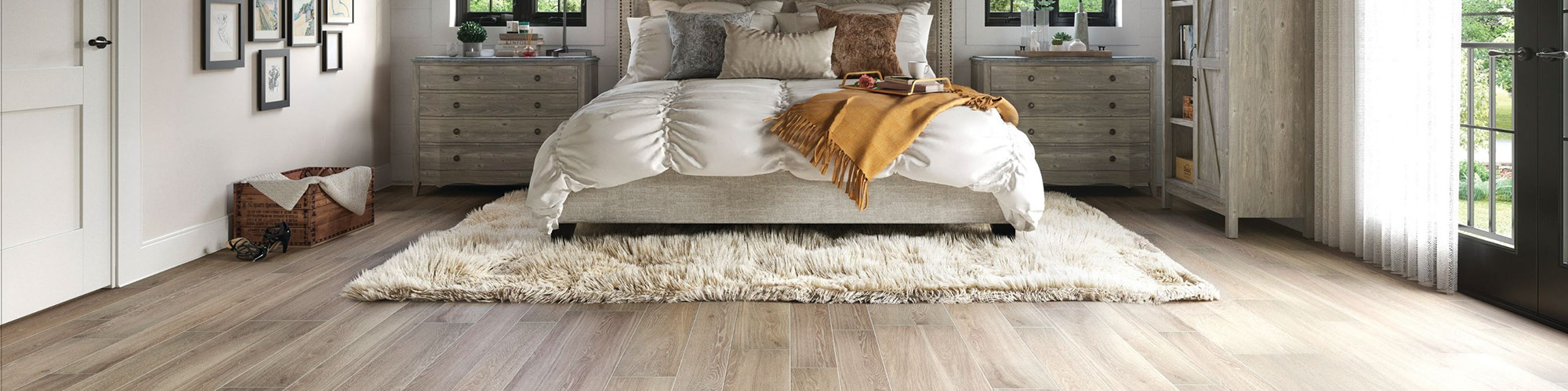 Modern farmhouse bedroom with floor tile that looks like wood, beige fuzzy rug under bed with white comforter & pillows, and gray wood nightstands.