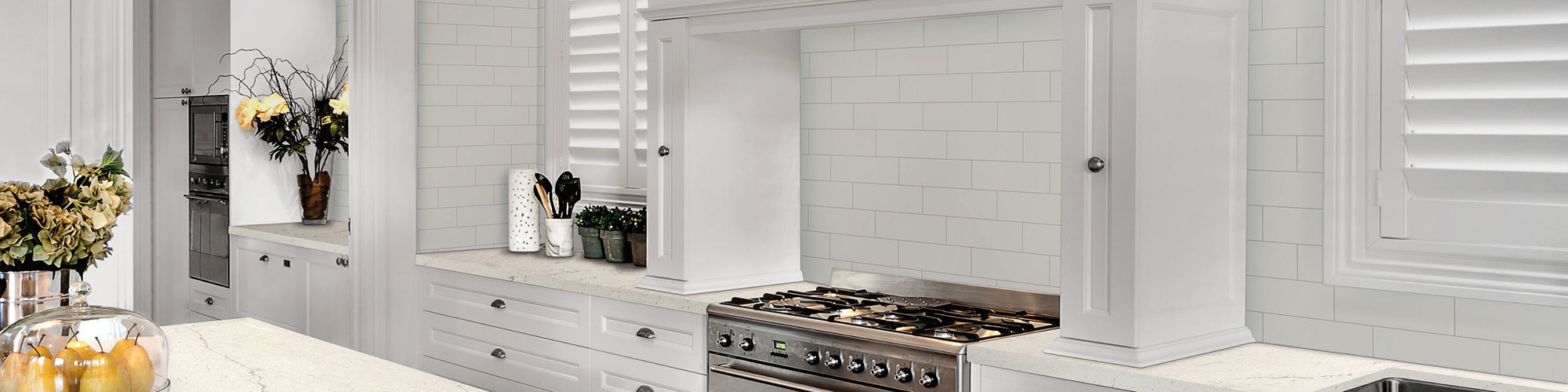 Fresh and clean kitchen décor with white subway tile backsplash, white quartz countertop & island, stainless steel gas stove, and white cabinets.