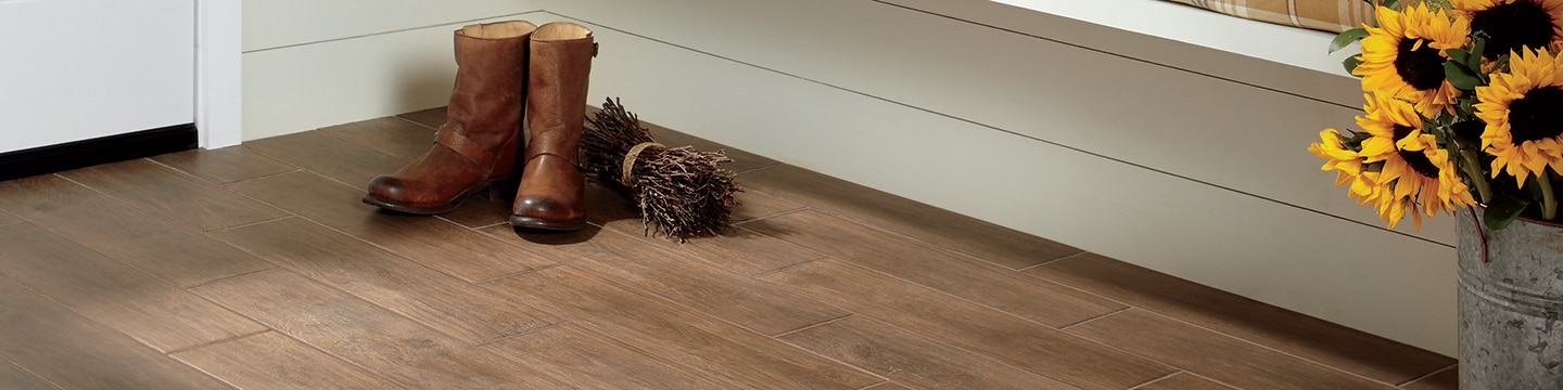 Mudroom with wood look tile flooring, white shiplap walls & bench, leather cowboy boots next to a bundle of hay and sunflowers in an aluminum can.