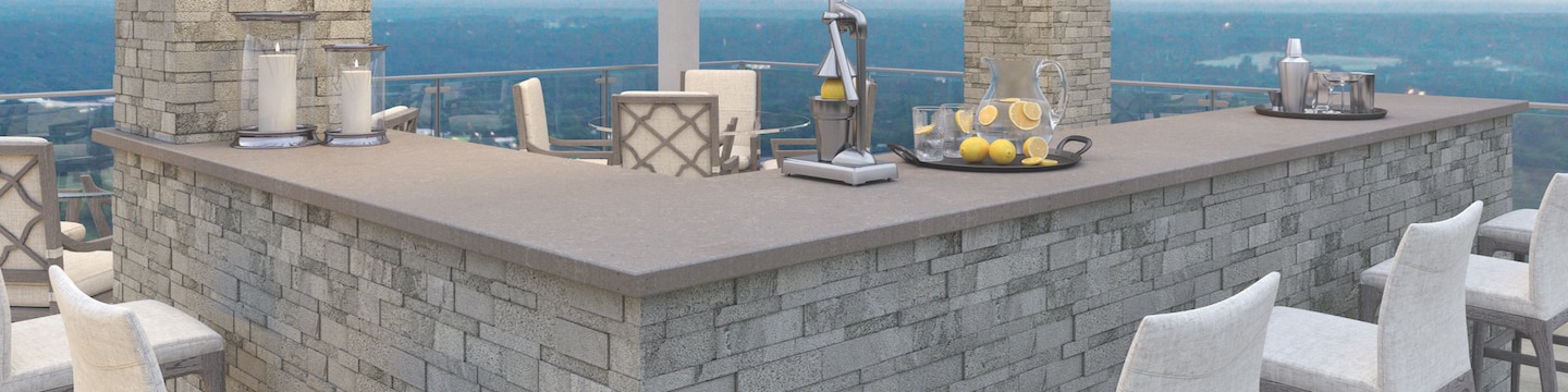Rooftop bar with gray countertop, gray stacked stone columns and bar base, and white bar stools.