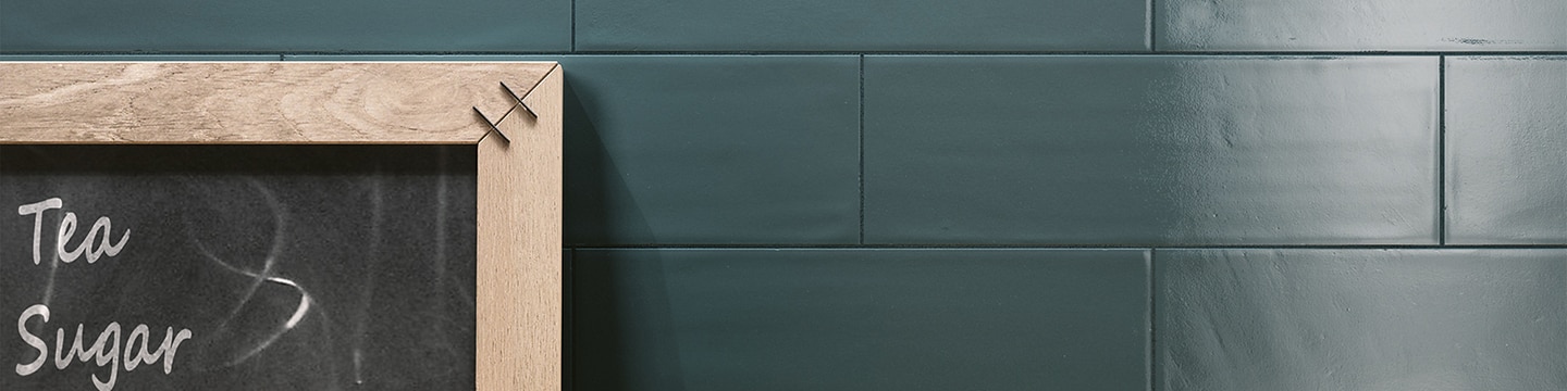 Closeup of deep teal subway tile with matching grout and chalkboard with wood frame.
