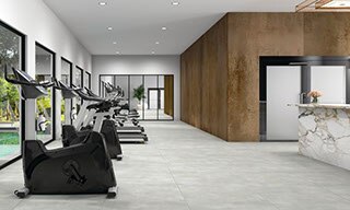 Hotel gym with a row of treadmills and stationary bicycles, stone look gray tile floor, metal look bronze wall tile, and white & gray marble look porcelain slab countertop.