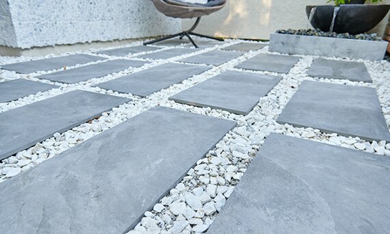 Closeup of outdoor patio of gray stone look 2CM porcelain pavers set in white gravel.