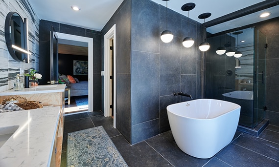 Freestanding bathtub with round pendant lighting, separate walk-in shower with dark gray stone look floor tile and wall tile, and white quartz counter.