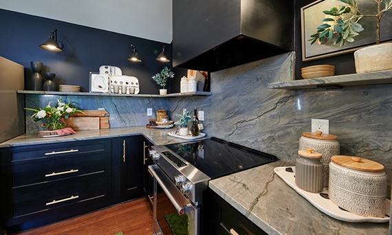 Kitchen with gray natural quartzite backsplash, floating shelves, and countertop, black lower cabinets, stainless steel stove, and black hood vent.