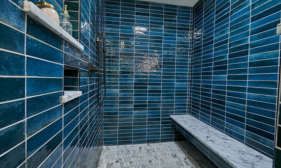 Shower with blue porcelain wall tile, bench of white & gray marble slab, marble elongated hex mosaic shower floor tile.