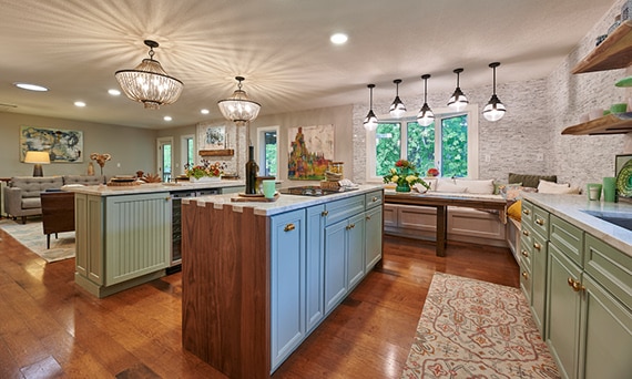 Open living and kitchen with double kitchen islands with natural quartzite countertops, wood & mint lower cabinets with brass handles, and dual chandeliers.