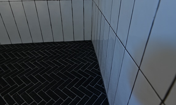 Closeup of black chevron mosaic shower floor tile with white grout and white vertical shower wall tile with black grout.