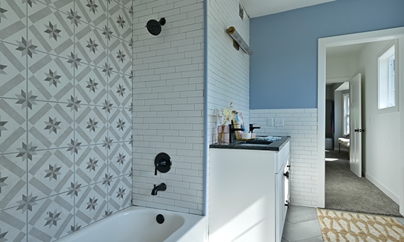 Bathroom with white subway and gray encaustic shower tile, black soapstone countertop on white vanity.